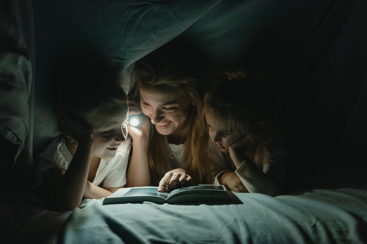 Adult and children reading with a flashlight under a blanket