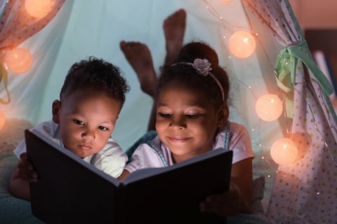 Children reading in indoor tent by the glow of a string of lights