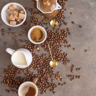 Coffee beans on a table that is set with coffee, cups, and creamer