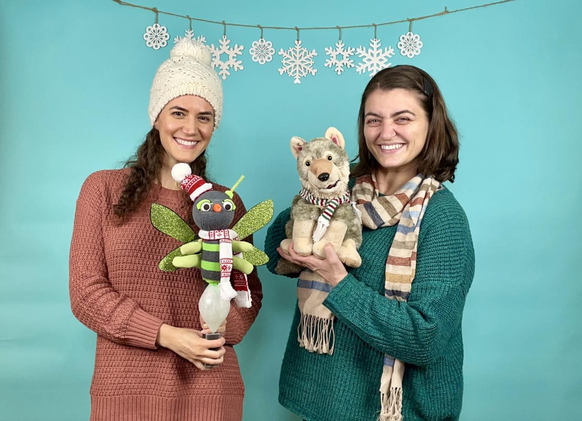 Two women in winter gear, each holding a puppet